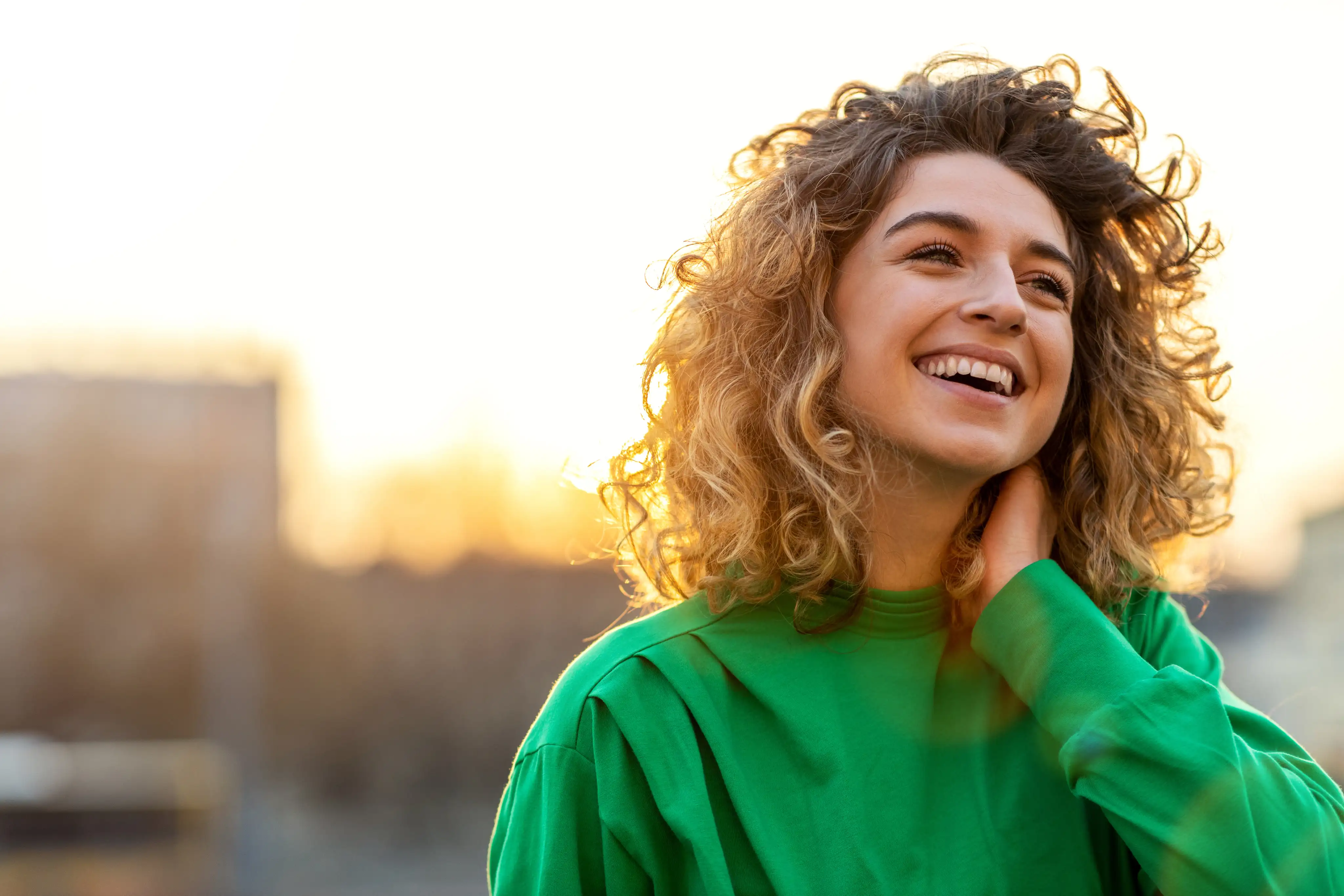 Young adult woman in a green shirt, smiling at sunset.