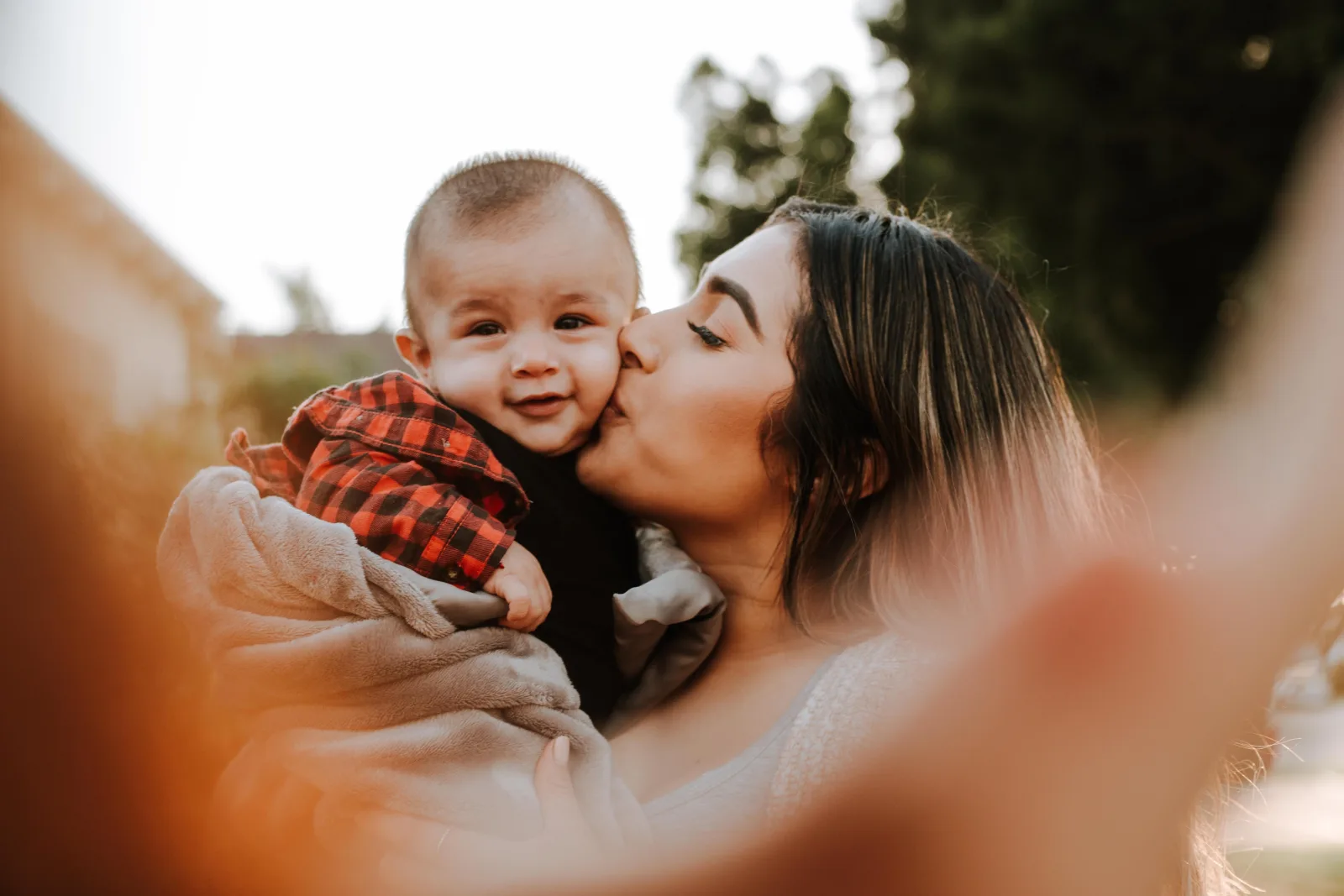 A young mother kisses the check of her smiling baby.