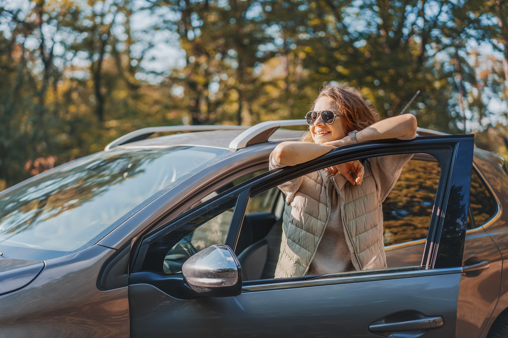 A woman smiles standing outside her parked car